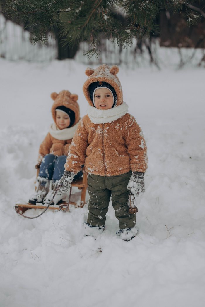 Services Two children in bear costumes playing with a sled in the snow during winter.