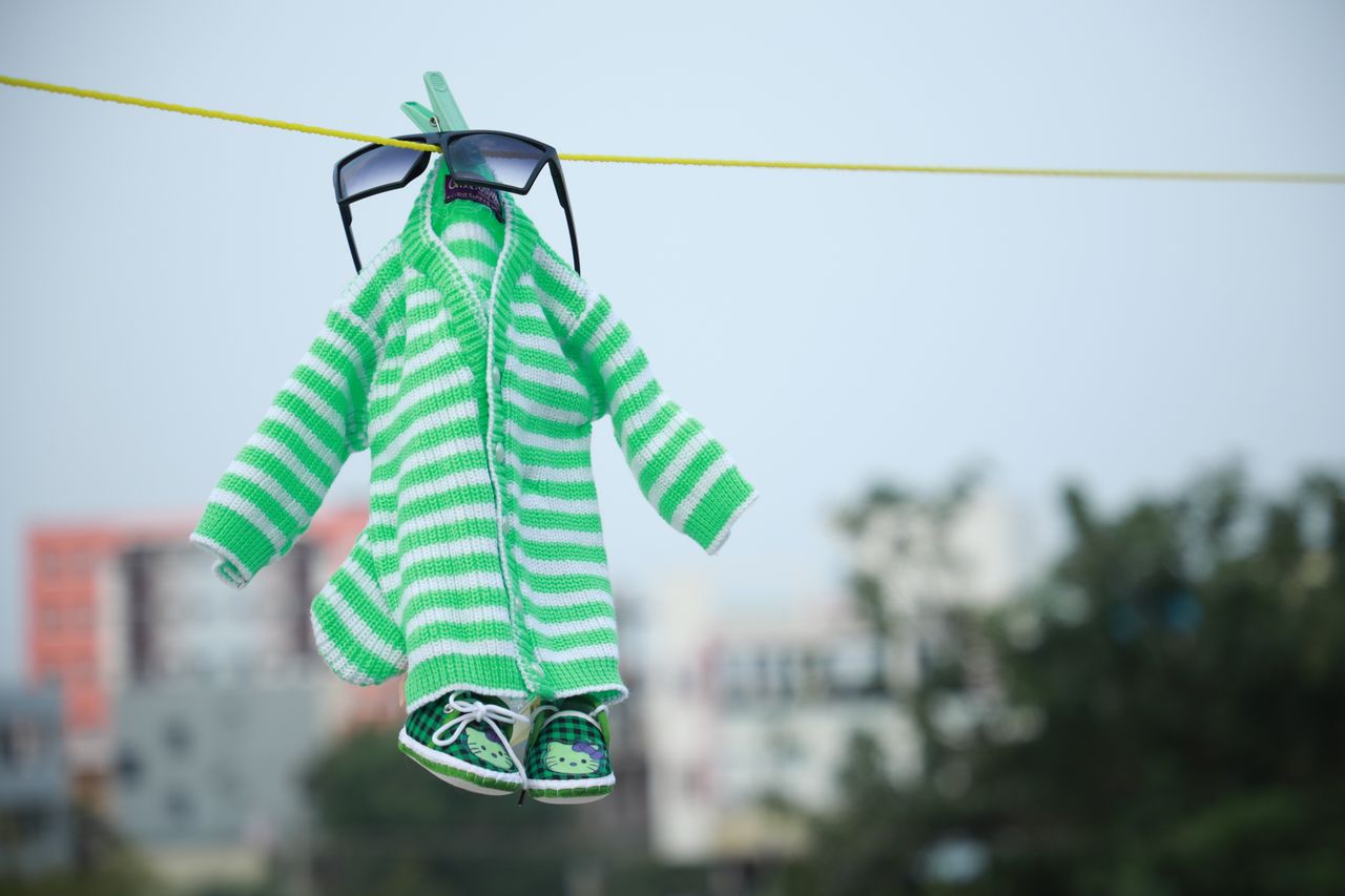 Services Cute green striped baby outfit with sunglasses hanging outdoors on clothesline.