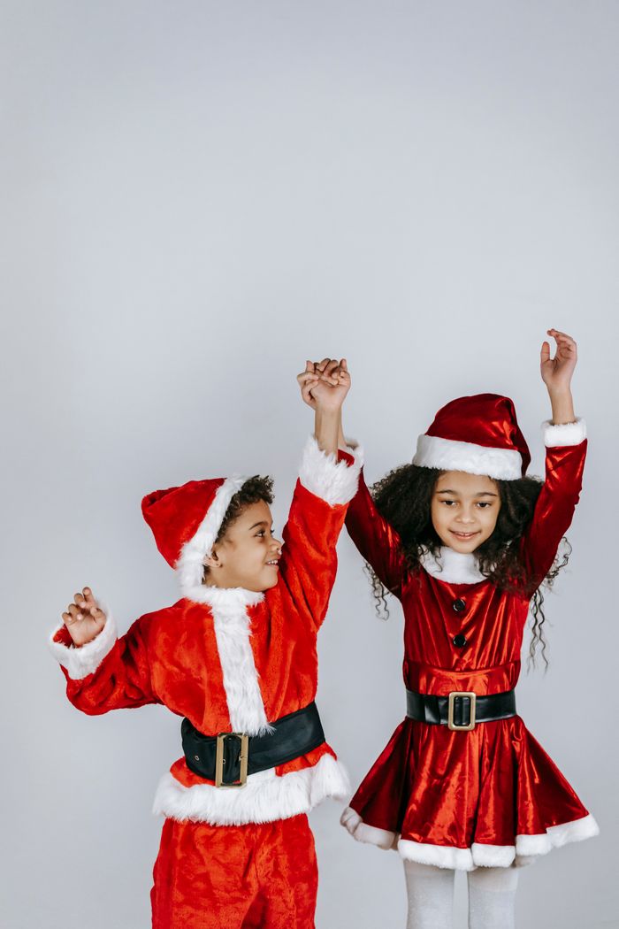 Mastering the First Impression: Your intriguing post title goes here Charming African American siblings in bright Santa costumes holding hands while having fun during New Year holiday on light background
