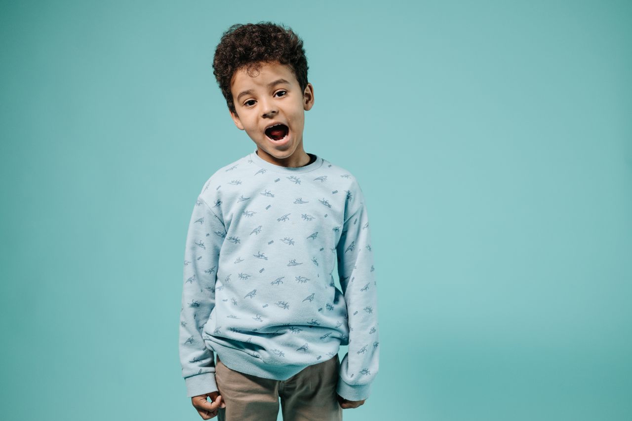Services Cheerful child in a blue sweater smiling against a turquoise backdrop.